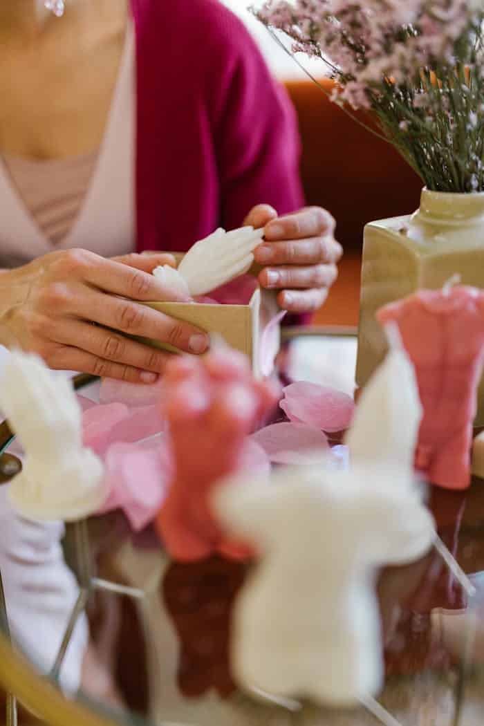 Close-up of hands crafting unique body-shaped candles with flowers in a home business setting.